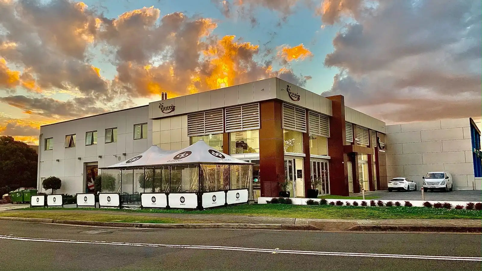 Commercial building with white walls and outdoor dining umbrellas at sunset.