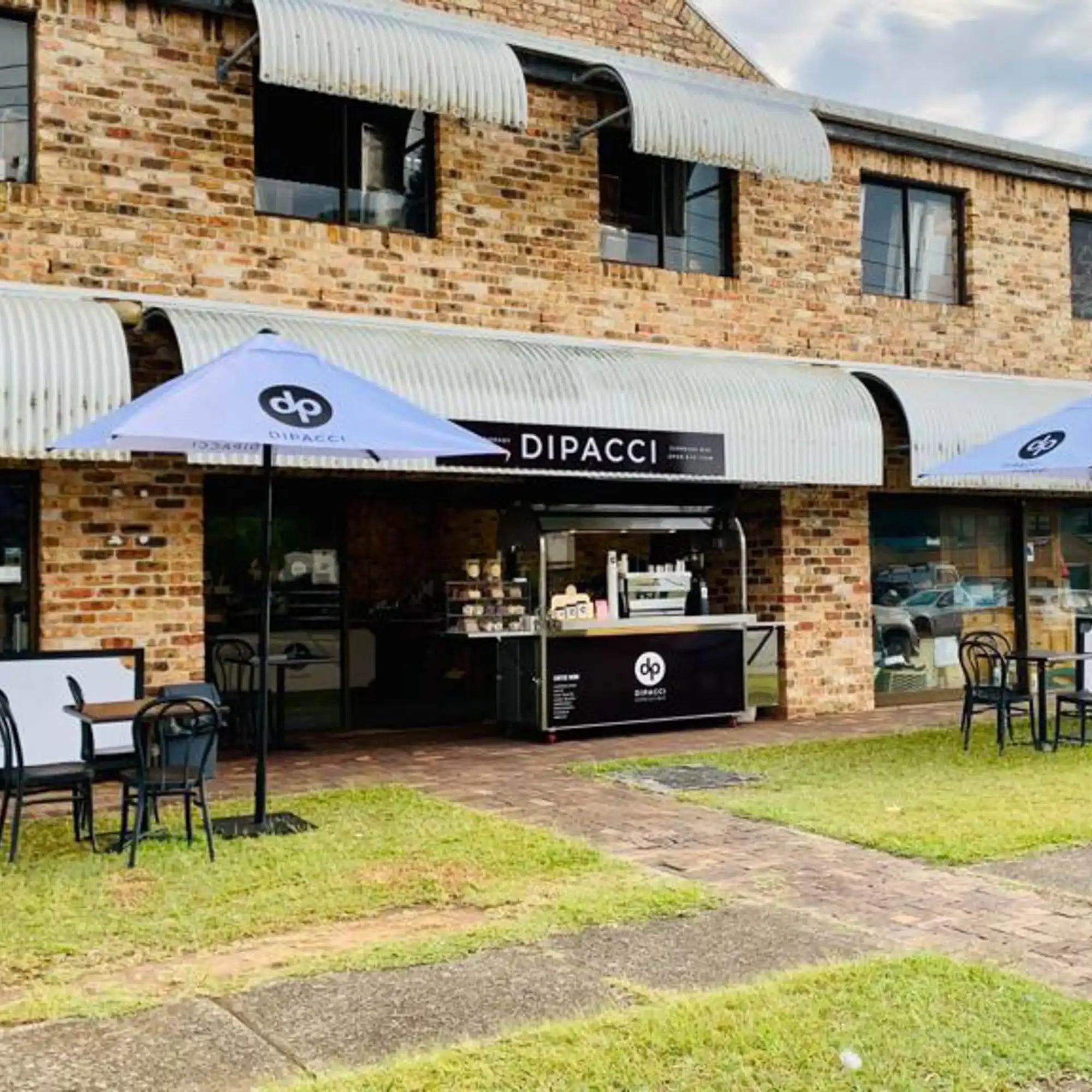 Dipacci coffee shop storefront with white awnings and branded umbrellas.