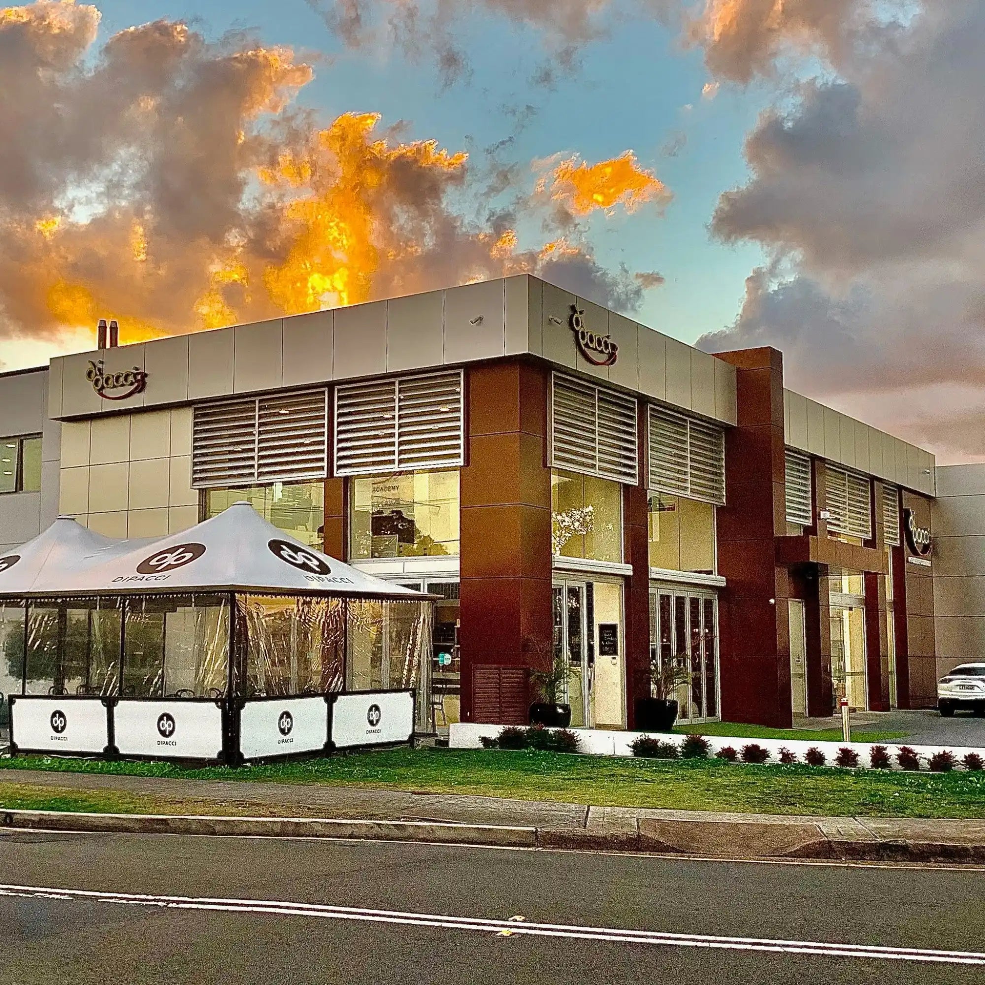 Modern restaurant building with white outdoor seating umbrellas and glass storefront.